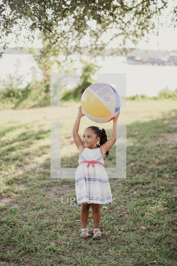 A little girl holding a beach ball over her head.