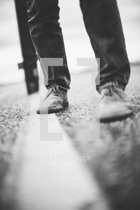 a man's feet on the pavement as he carries a large cross re-enacting Christ's walk, bearing the cross