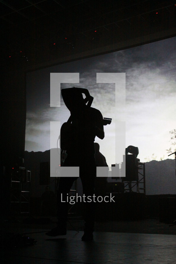 silhouette of a man on stage putting his guitar over his shoulder 