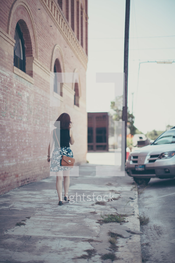 a woman with a purse walking down a sidewalk alone 