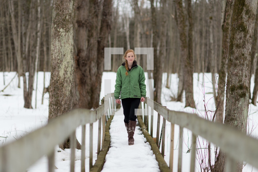 a teen girl walking on a bridge outdoors in snow 