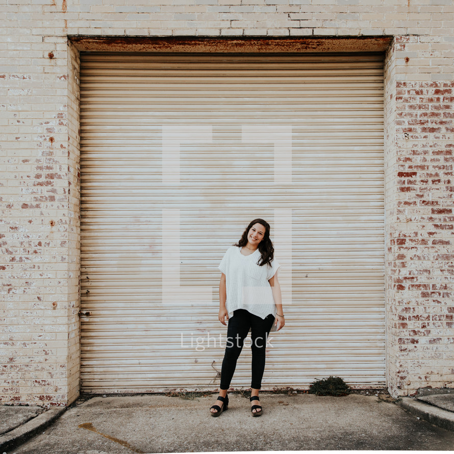 a woman standing in front of a warehouse garage door 