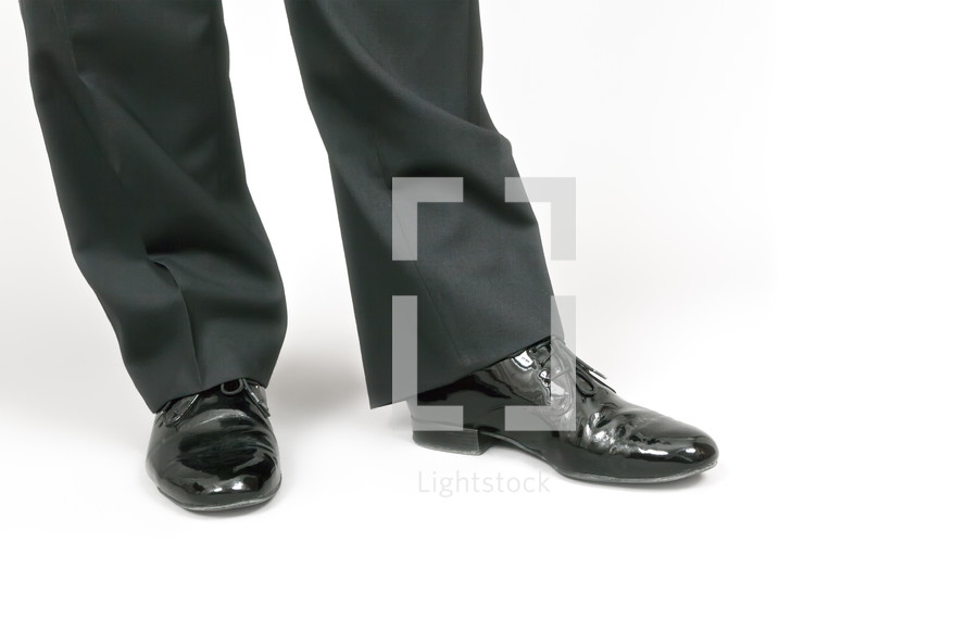 A man's feet in shiny black dress shoes.