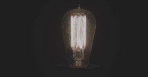 Vintage light bulb pulses and flickers in and out in dark room