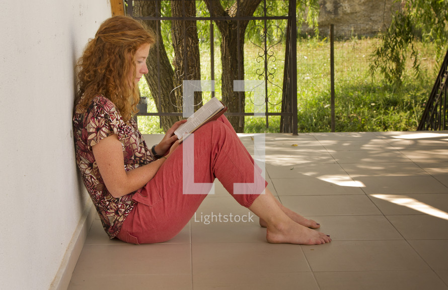 woman leaning against a wall reading a Bible 