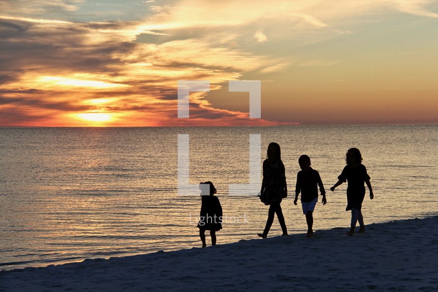 silhouettes of children playing on a beach at sunset 