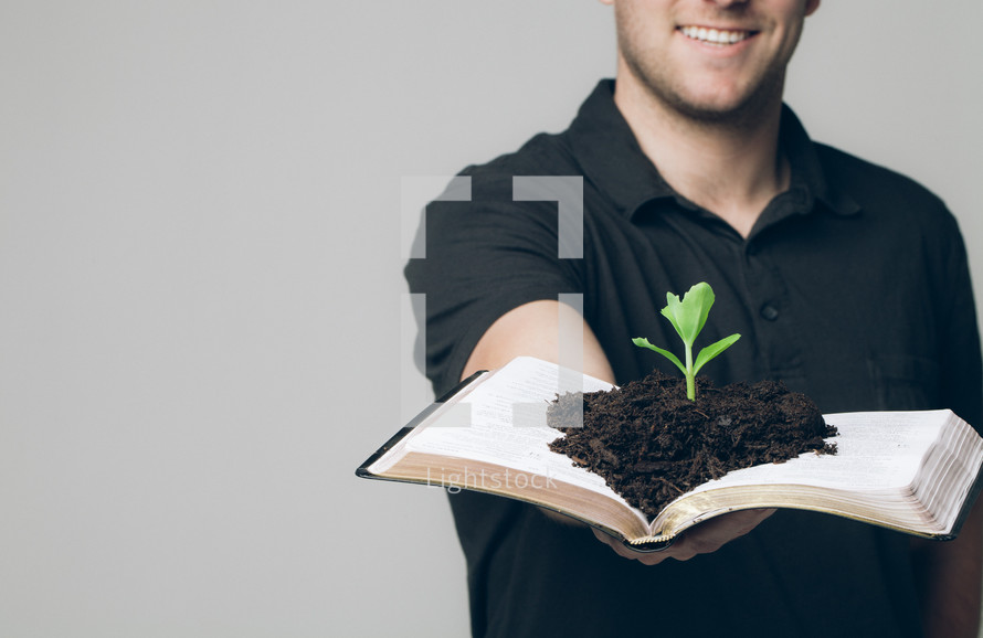 soil and a plant growing from the pages of a Bible