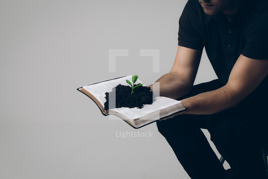 man holding a Bible with soil and a plant growing from its pages