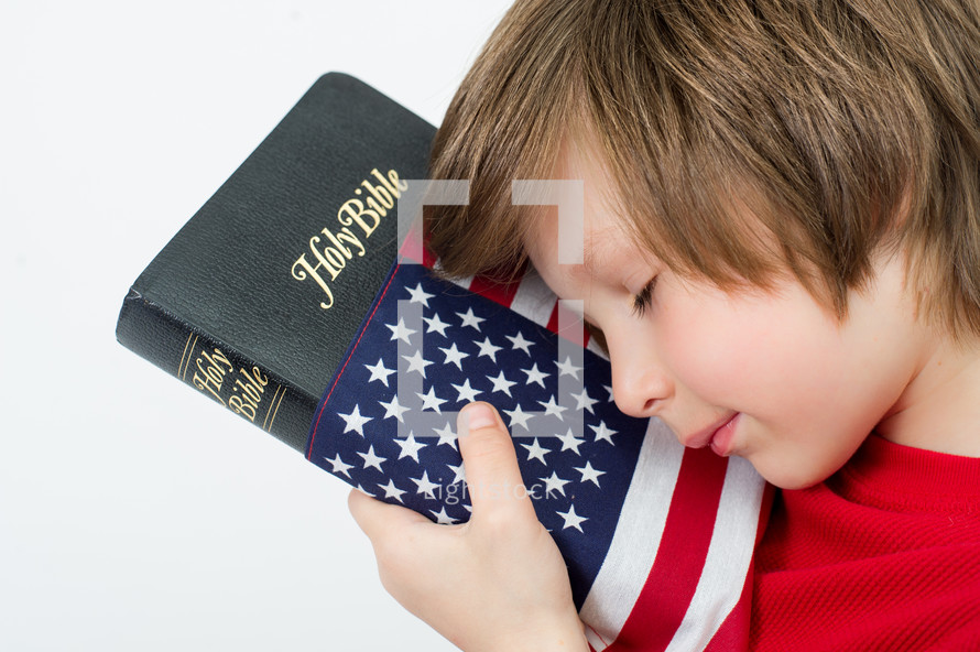 Boy praying over a Holy Bible wrapped in an American flag.