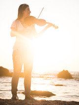 Beautiful woman wearing jeans playing the violin on a beach.