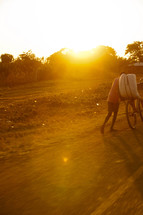 A man pushing a bicycle in Malawi, Africa under intense sunlight. 