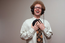A laughing man in headphones holding a vinyl record to his chest.