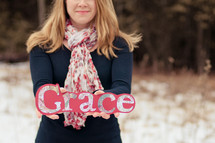 Woman standing outside in the snow holding a grace sign.