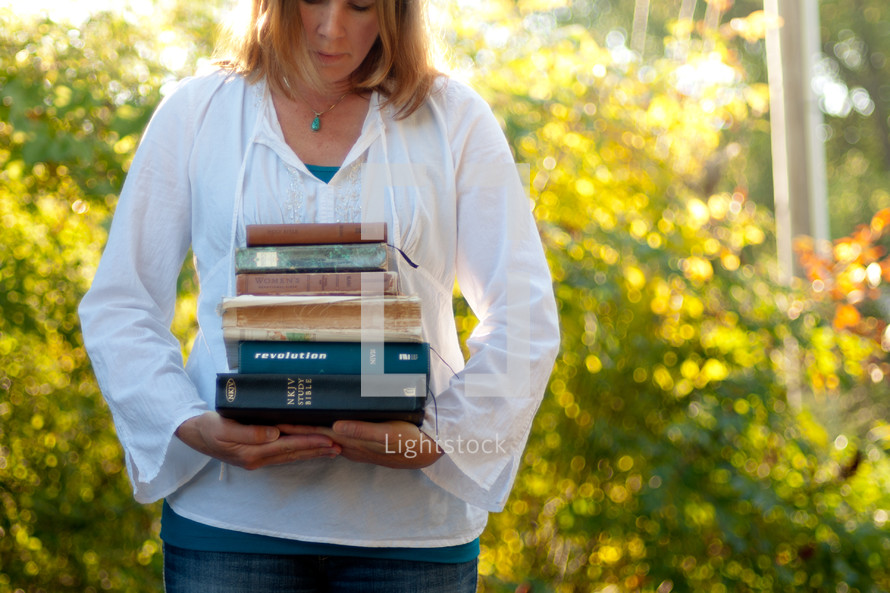 woman holding a stack of books outdoors 