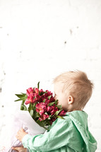 Boy smelling a bouquet of flowers.