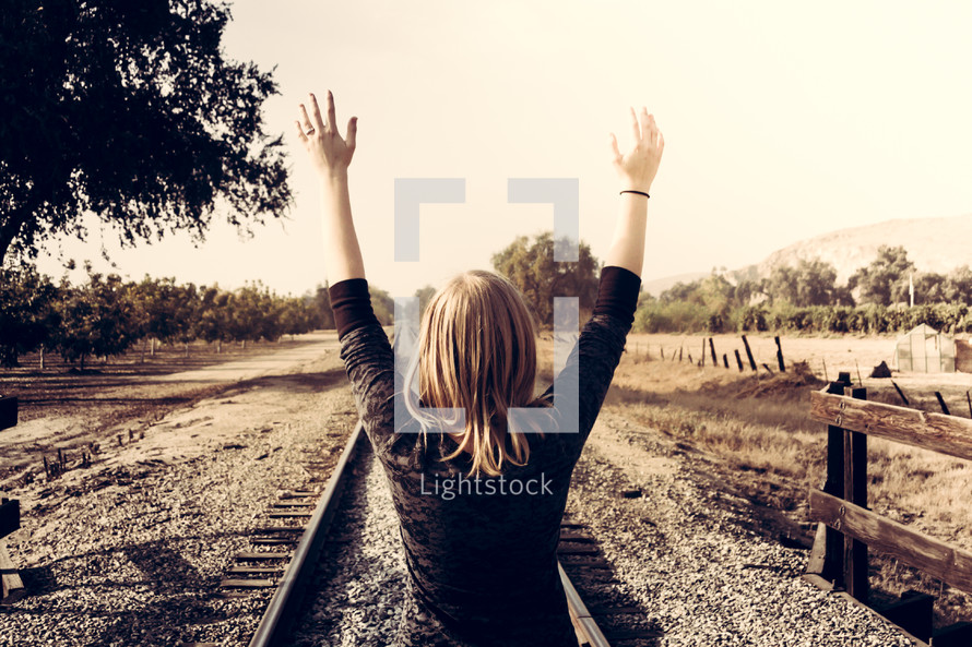 woman with arms raised standing on railroad tracks 
