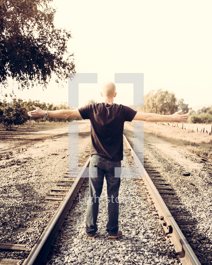 man with open arms on railroad tracks 