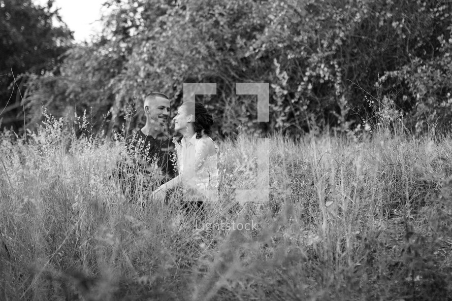 Couple, sitting and embracing each other in a weedy field 