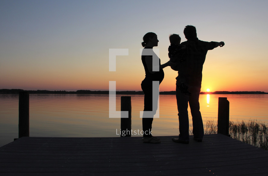 Silhouette of a family on a pier by the water at sunset.