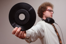 A man wearing headphones and holding out a vinyl record.
