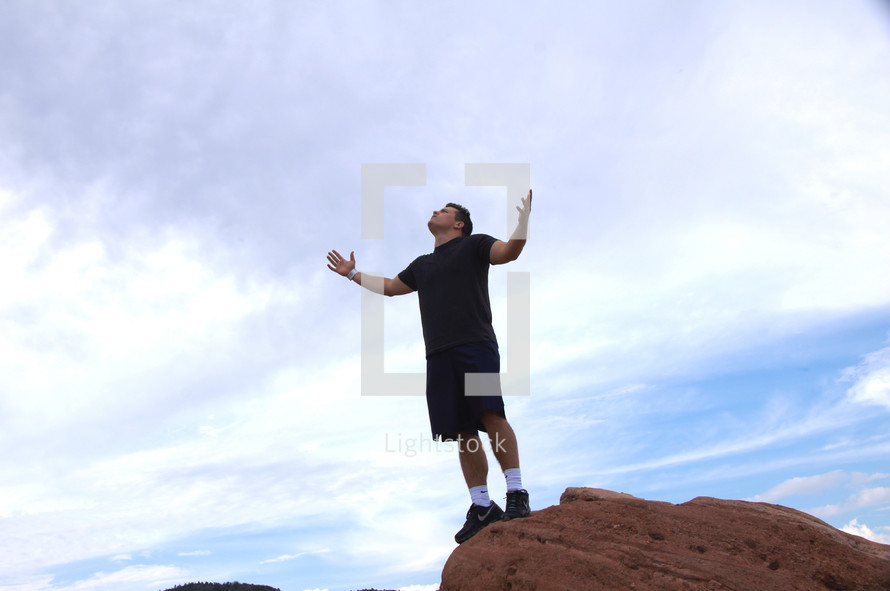 man standing on a red rock with arms raised