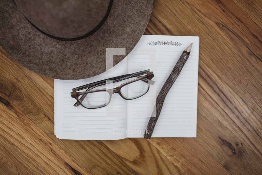 reading glasses, hat, pencil, and notebook on a wood floor 
