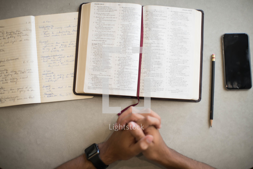 a man with praying hands in front of an opening Bible 