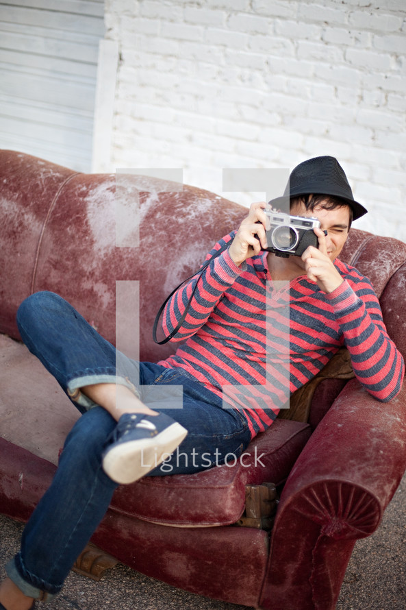 man sitting on an old couch outdoors taking a picture with a camera