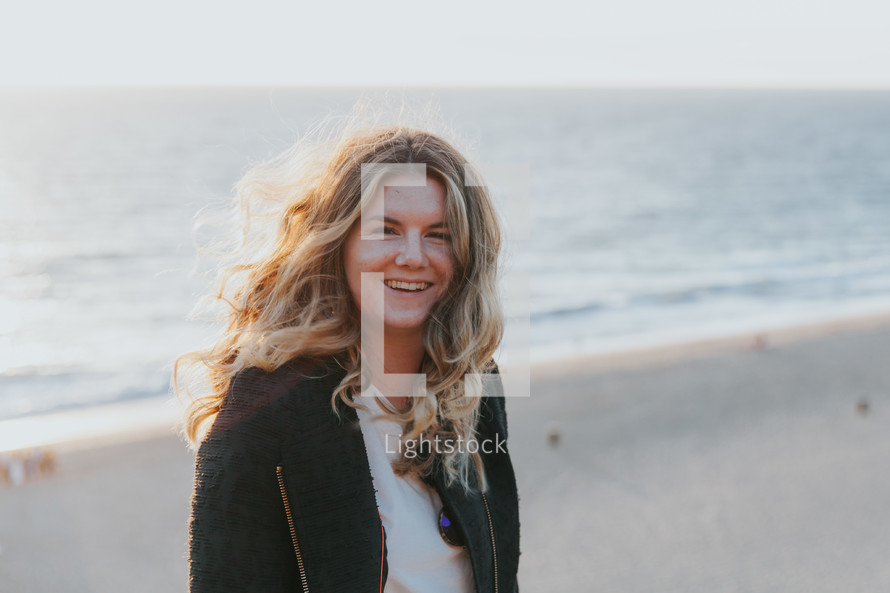 smiling woman in a sweater standing on a beach 