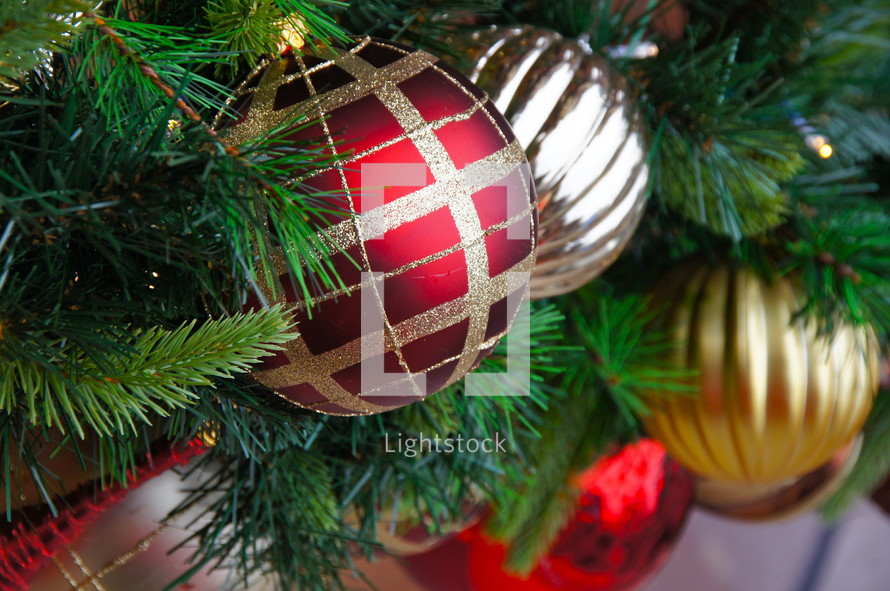 Red and gold ball Christmas ornaments hanging from pine Christmas tree.