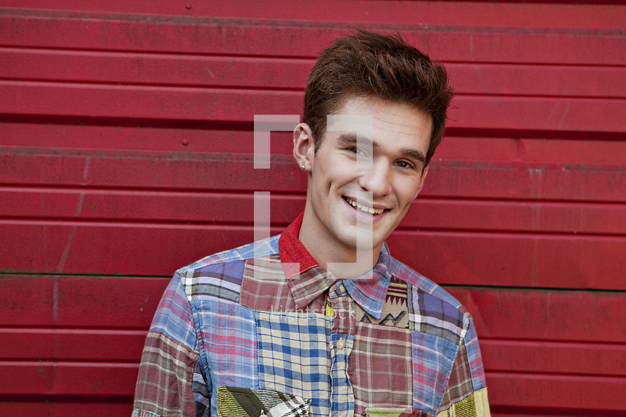 man in plaid standing in front of a red wall smiling