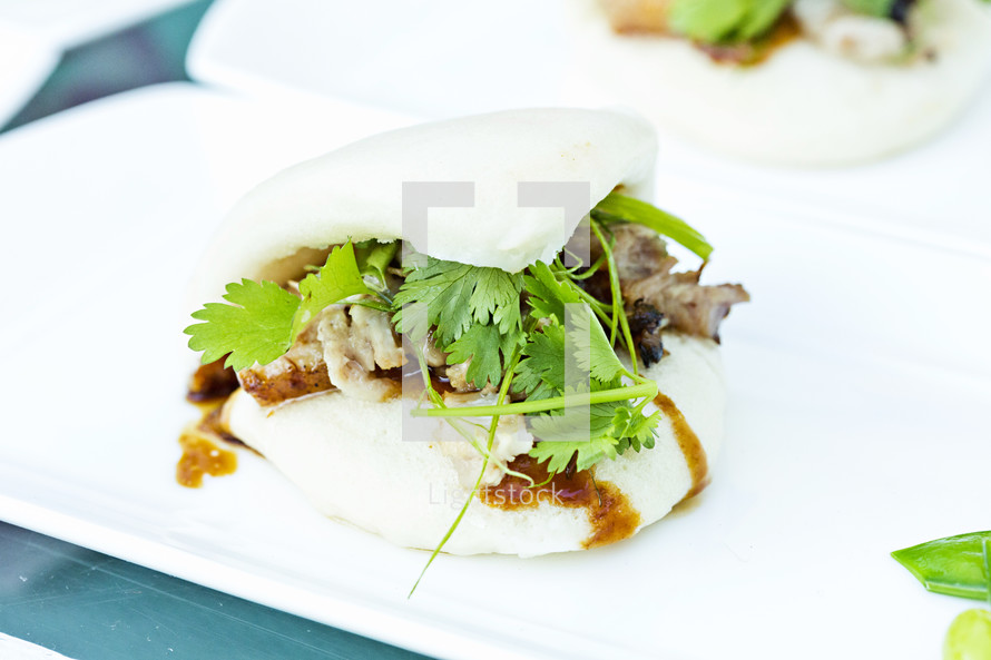 Pork belly  and cilantro present on white plate food. 