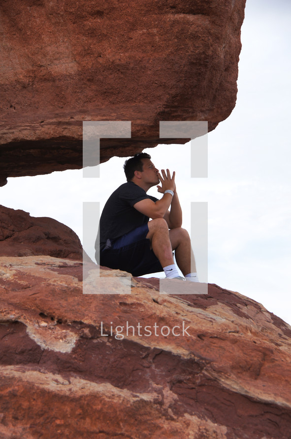 Man praying and in deep thought on a red rock at the top of a mountain