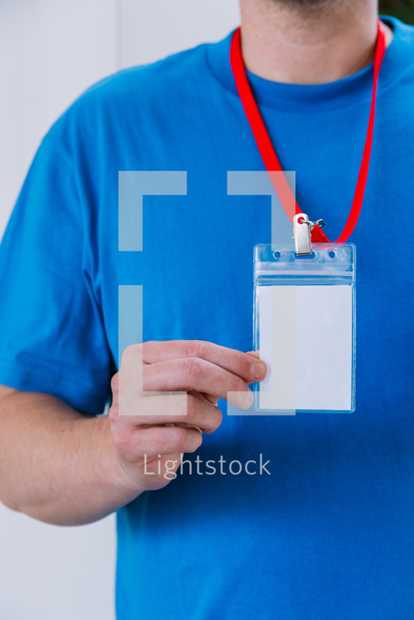 Close up of a man in a blank blue tshirt holding up a lanyard.