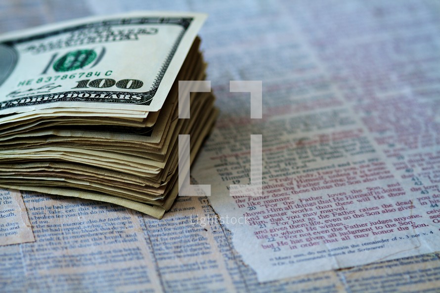 A stack of one hundred dollar bills sits on pages of scripture.