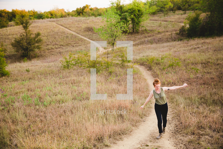 woman walking on a path up a hill with open arms 