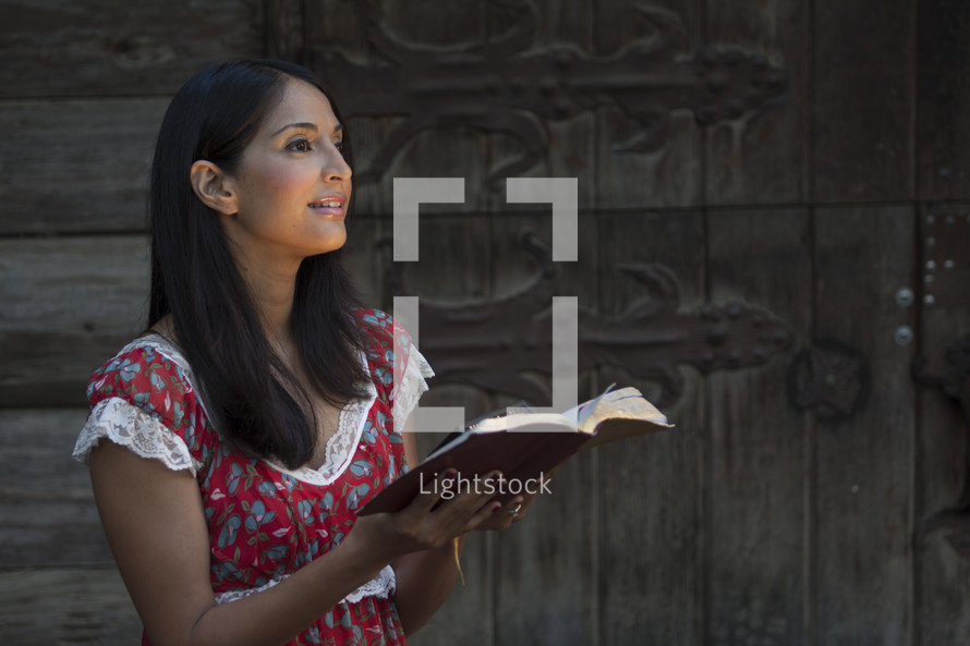 Woman holding Bible in front of wooden doors.