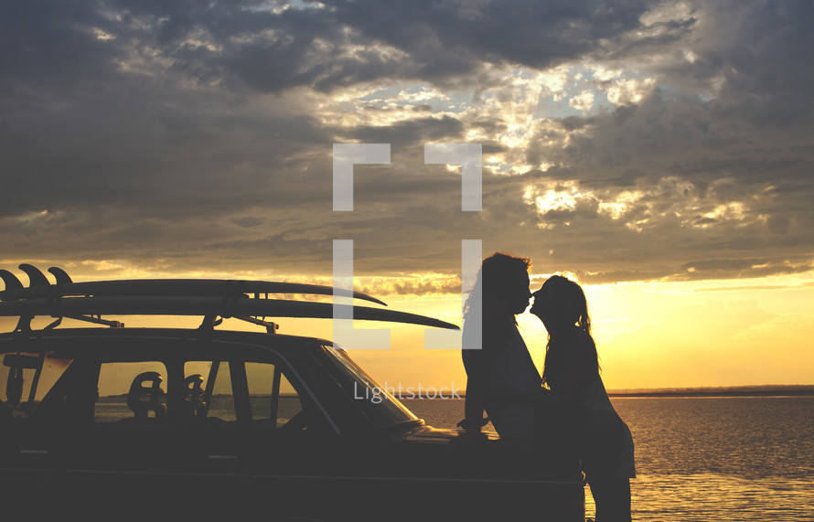 a couple leaning on a car about to kiss at sunset
