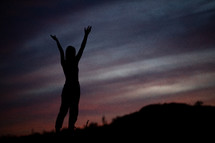 silhouettes of young women on a mountaintop at sunset with hands raised 