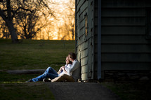 couple sitting together against a barn outdoors at sunset 