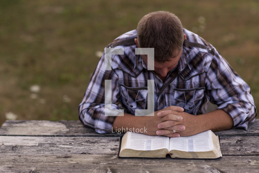 a man praying over the pages of a Bible outdoors 