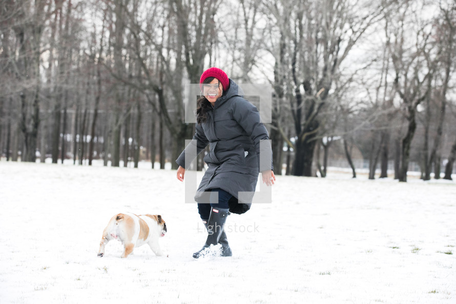a smiling woman playing in snow with a bulldog 