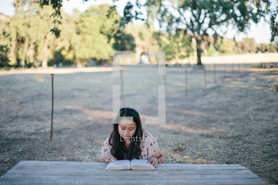 woman reading a Bible at a picnic table 