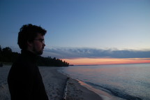 A man looks at a lake at sunset.