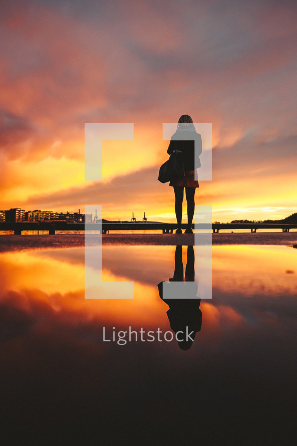 reflection of a woman at sunset on wet sand on a beach 