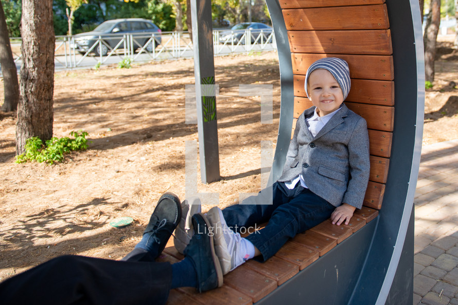 a sweet little boy sitting in a park in dress clothes 