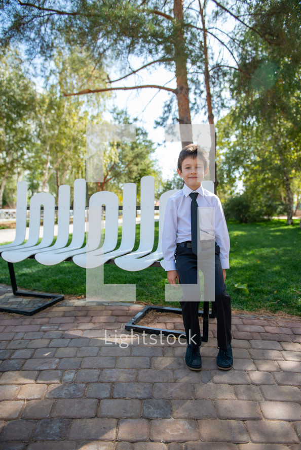 portrait of a boy in dress clothes sitting on a bench in a park 