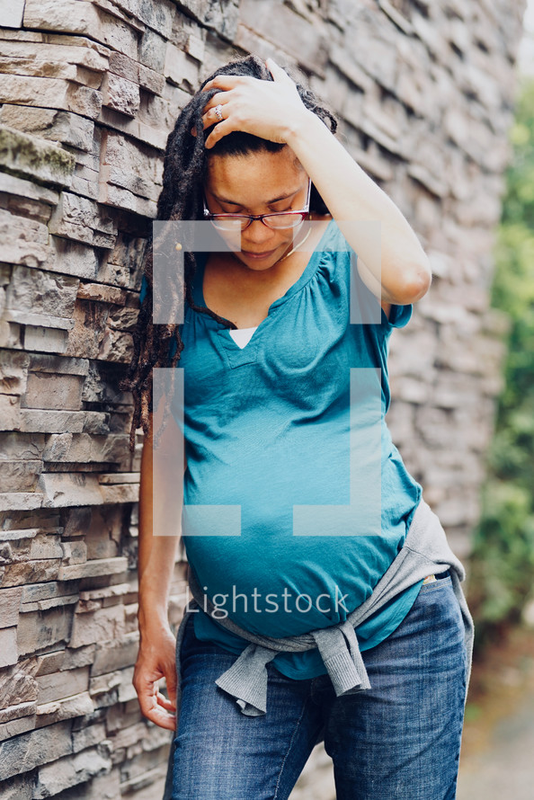 Pregnant African-American Woman leaning against an exterior stone wall
