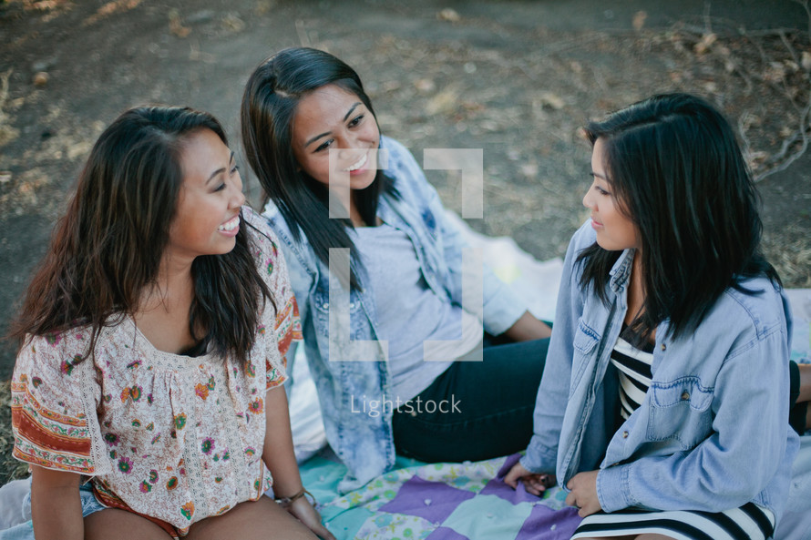 friends sitting on a blanket outdoors talking 