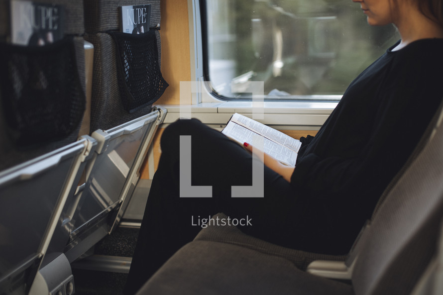 A girl sitting on a train a train reading her bible. 